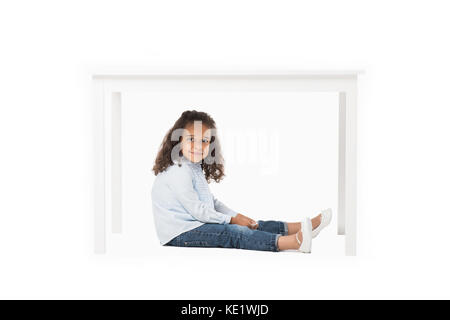 Adorabili americano africano ragazza seduta sotto la tabella isolato su bianco Foto Stock