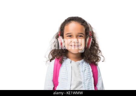 Adorable African American schoolgirl ascoltando musica in cuffia e sorridente in telecamera isolato su bianco Foto Stock