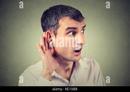Closeup ritratto di udito collocando man mano sull'orecchio chiedere a qualcuno di parlare o ascoltare attentamente un gossip isolato sul muro grigio backgroun Foto Stock