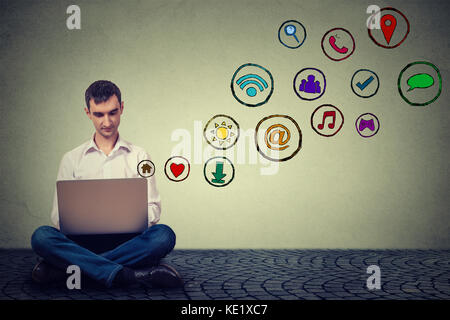 Giovane uomo che lavora utilizzando laptop seduto su un pavimento social media le icone delle applicazioni battenti fino. una moderna tecnologia di comunicazione concept Foto Stock