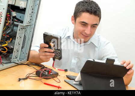 Un giovane tecnico che lavora su computer rotto con la compressa Foto Stock
