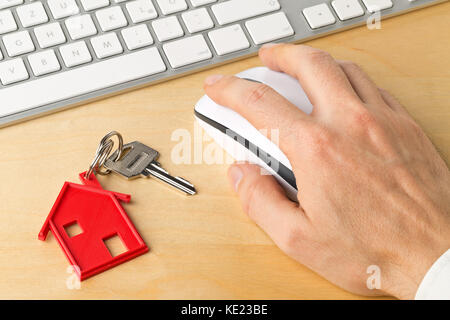 Casa porta chiave con red house chiave catena pendente e uomo utilizzando computer sulla scrivania in legno - casa online il noleggio o acquisto di concetto Foto Stock