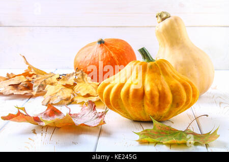 Zucca e Patty pan e acero, rovere foglie gialle su una bianca tavolo in legno. raccolto autunnale. Foto Stock