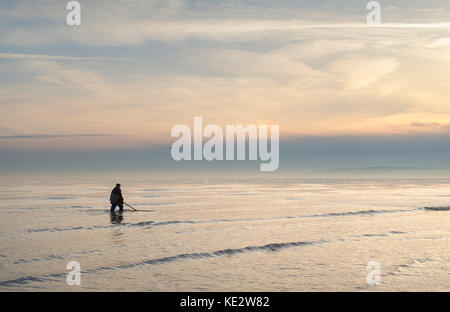 Un pescatore di passeggiate in riva al mare al tramonto sulla costa del Kent Foto Stock