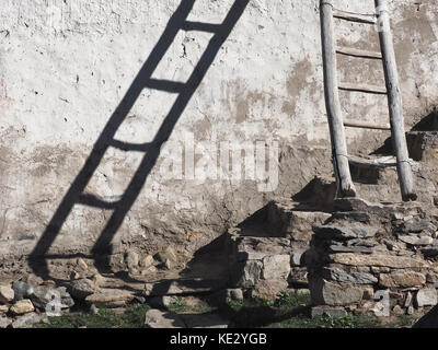 Vecchia scalinata in legno che è appoggiata contro una parete bianca, un ombra dalle scale cade sulla parete, pietre nel seminterrato, un design interno moderno pho Foto Stock