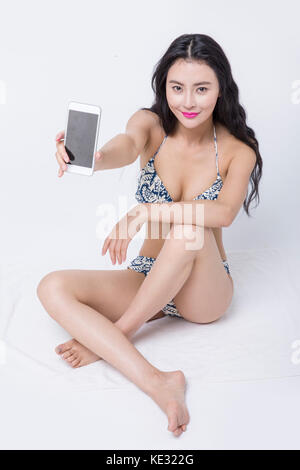 Giovane donna sorridente in bikini in posa con uno smartphone Foto Stock
