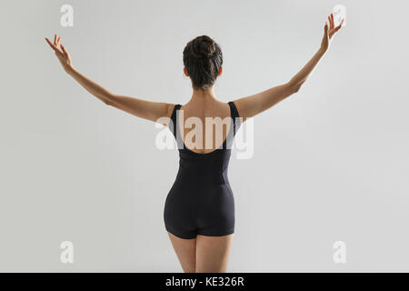 Retro del giovane ballerina in nero leotard apertura ponendo le braccia Foto Stock