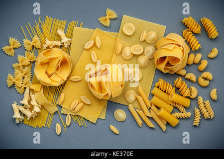 Cibi italiani concept e design menu. un assortimento di tipi di farfalle, pasta un riso, orecchiette pugliesi, gnocco sardo e farfalle setup su grigio Foto Stock