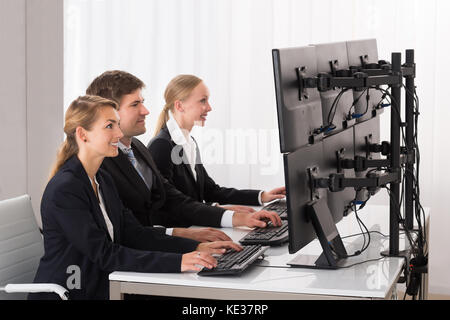 Happy businessman lavorando su più computer in ufficio Foto Stock
