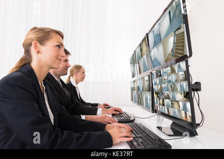 Maschi e femmine di sicurezza agli operatori di sistema guardando video TVCC su più computer Foto Stock