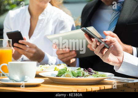 Close-up di imprenditori con tavoletta digitale e il telefono cellulare con il cibo sulla tavola Foto Stock