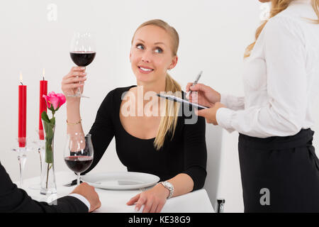 Cameriera prendendo un ordine da un paio di bere un bicchiere di vino rosso Foto Stock