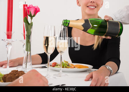 Primo piano della cameriera femmina versando Champagne in vetro per la felice coppia giovane nel ristorante Foto Stock