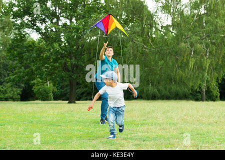 Padre esegue dopo i battenti colorato aquilone attesa da suo figlio nel Parco Foto Stock