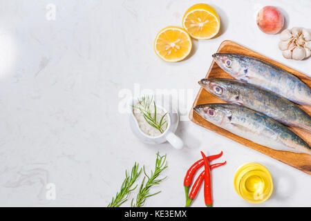 Piatto di pesce in cucina con vari ingredienti. fresco pesce crudo decorate con le fette di limone e le erbe sul tavolo di legno. Foto Stock