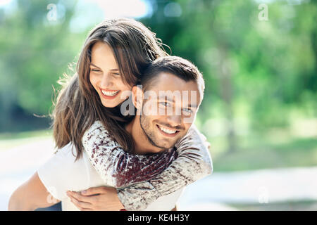 All'esterno ritratto di felici gli amanti del giovane uomo e donna che guarda la fotocamera. Ragazza sorridente piggyback del fidanzato. Amore, gioventù, concetto di relazione ph Foto Stock