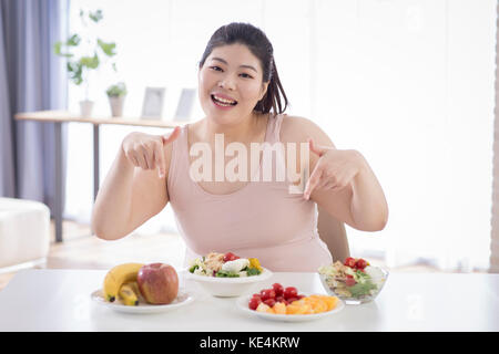 Ritratto di giovane sorridente donna grassa puntando alla frutta e verdura Foto Stock