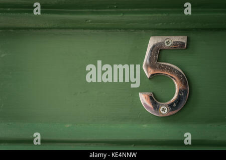 Un weathered chrome numero 5 avvitata ad una porta verde nel Regno Unito. Foto Stock