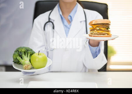 Ritratto di medico donna azienda frutta, verdura e fast food Foto Stock