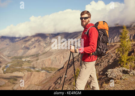 Bel giovane maschio barbuto escursionista in piedi sul bordo di un canyon che guarda lontano Foto Stock