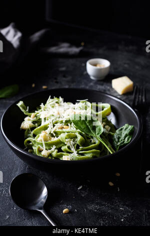 Gli spinaci verde la pasta con il formaggio e i pinoli in una ciotola nero con nero posate. gourmet pasto italiano. vista laterale Foto Stock