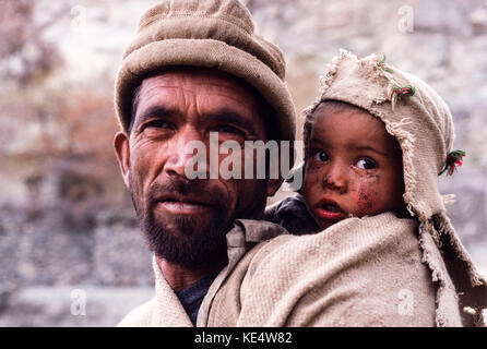 Baltistan, Pakistan, 1990; un pastore Balitsani porta il suo giovane figlio sulla sua schiena come egli cammina attraverso le montagne vicino a Skardu. Foto Stock