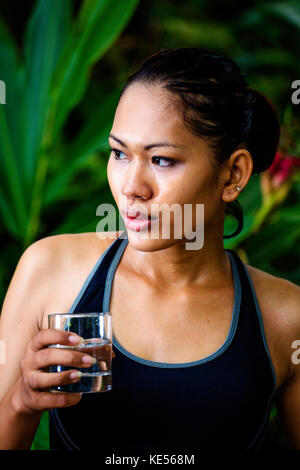 Donna asiatica in abiti di fitness con un bicchiere di acqua Foto Stock
