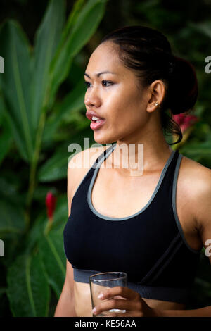 Donna asiatica in abiti di fitness con un bicchiere di acqua Foto Stock