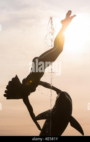 " Ragazza con un delfino' scultura, stagliano contro il Rising Sun, London, Regno Unito Foto Stock