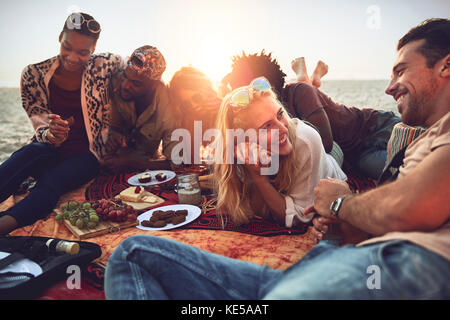 I giovani amici si divertono a fare un picnic sulla soleggiata spiaggia estiva Foto Stock