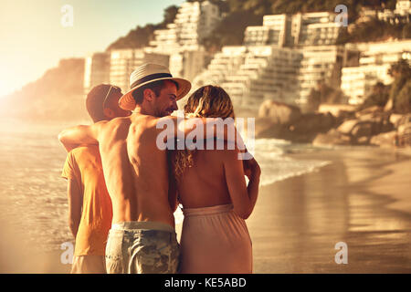 Amici giovani e affezionati che camminano sulla soleggiata spiaggia estiva Foto Stock