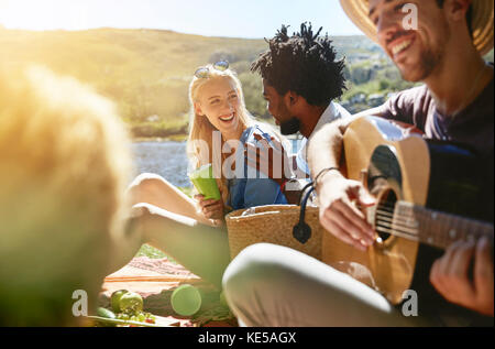 Giovani amici che suonano la chitarra e che si godono un picnic estivo soleggiato Foto Stock