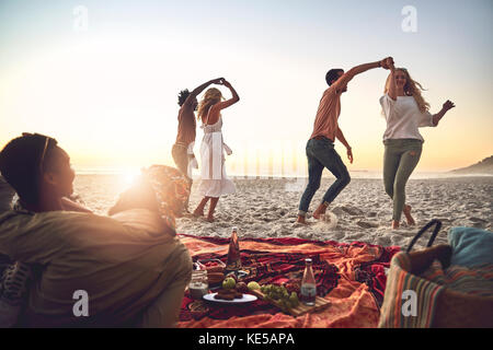 Giovani coppie che ballano, gustando un picnic sulla spiaggia estiva Foto Stock