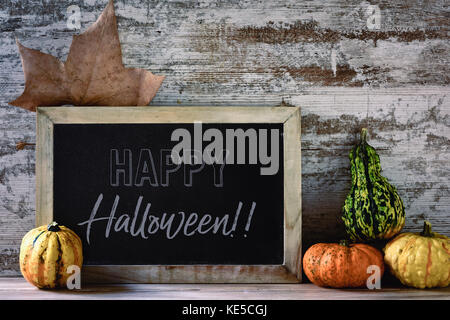 Un di legno-incorniciato lavagna con il testo happy Halloween, un autunno foglia e alcune diverse varietà di zucche su una tavola in legno rustico Foto Stock