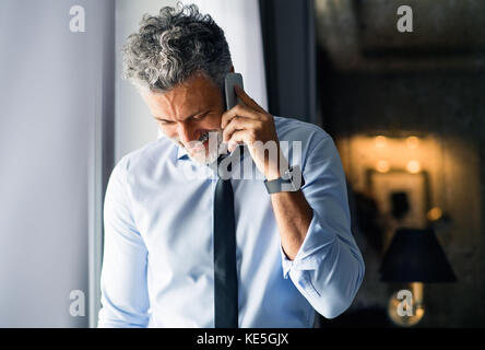 Imprenditore maturo con lo smartphone in una camera di hotel. Foto Stock