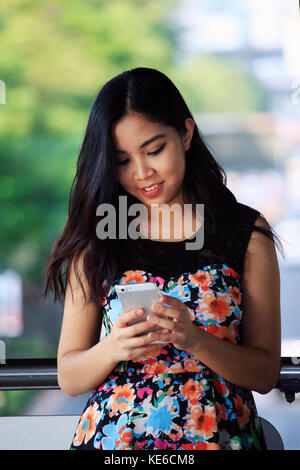 Giovane donna asiatica di messaggistica all'aperto sullo smartphone Foto Stock