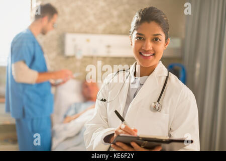 Ritratto sorridente dottore che fa giri, prendendo appunti sulla cartella clinica appunti in camera d'ospedale Foto Stock