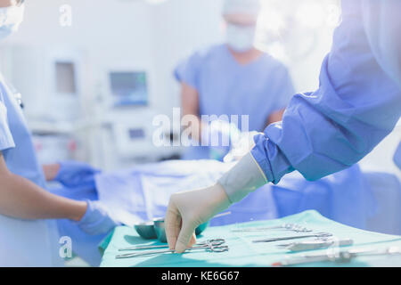 Il chirurgo in guanti di gomma raggiunge le forbici chirurgiche sul vassoio in sala operatoria Foto Stock