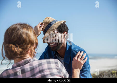 Divertente coppia multietnica con cappello sulla soleggiata spiaggia estiva Foto Stock