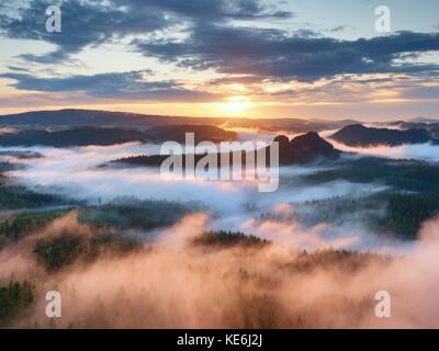 Pink sunrise in una bellissima pietra arenaria Rocky Mountain. picchi aguzzi aumentato da sfondo velato, la nebbia è di colore rosso e arancione a causa di sole caldo. Foto Stock