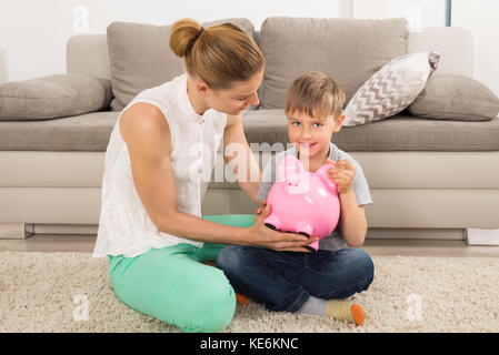 Madre e figlio seduti su un tappeto Holding Piggybank Foto Stock