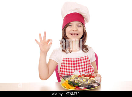 Felice bambina cook con trote e segno OK con la mano Foto Stock