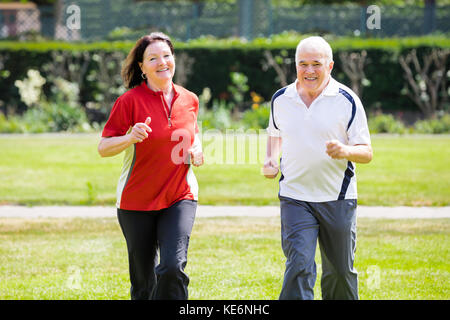Sorridente coppia Senior correndo insieme in posizione di parcheggio Foto Stock