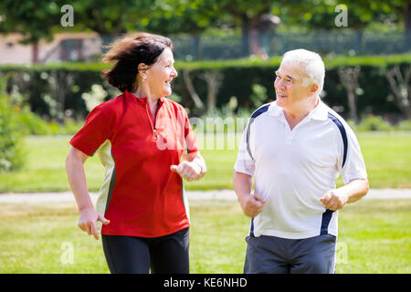 Sorridente coppia Senior correndo insieme in posizione di parcheggio Foto Stock