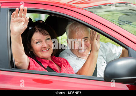 Felice coppia Senior seduta all'interno auto agitando addio Foto Stock