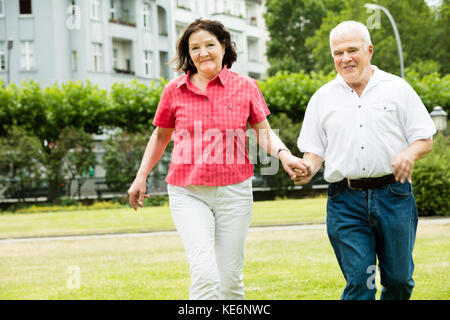 Felice coppia Senior in esecuzione in Park Holding Hands Foto Stock
