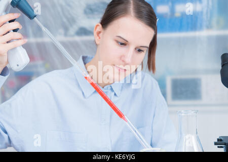 Donna scienziato aggiunge liquido al tubo di prova con una pipetta in laboratorio Foto Stock