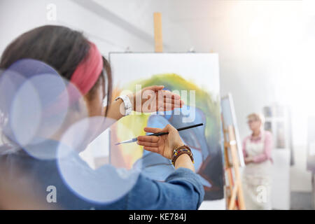 Donna artista gesturing, pittura incorniciante su cavalletto in studio di classe d'arte Foto Stock