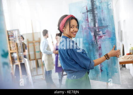 Ritratto sorridente artista femminile sollevamento pittura in studio di classe d'arte Foto Stock