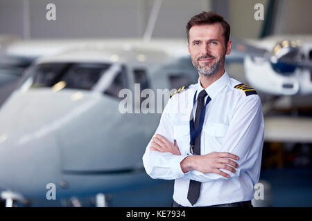 Ritratto fiducioso pilota maschio in piedi vicino in aereo in hangar Foto Stock